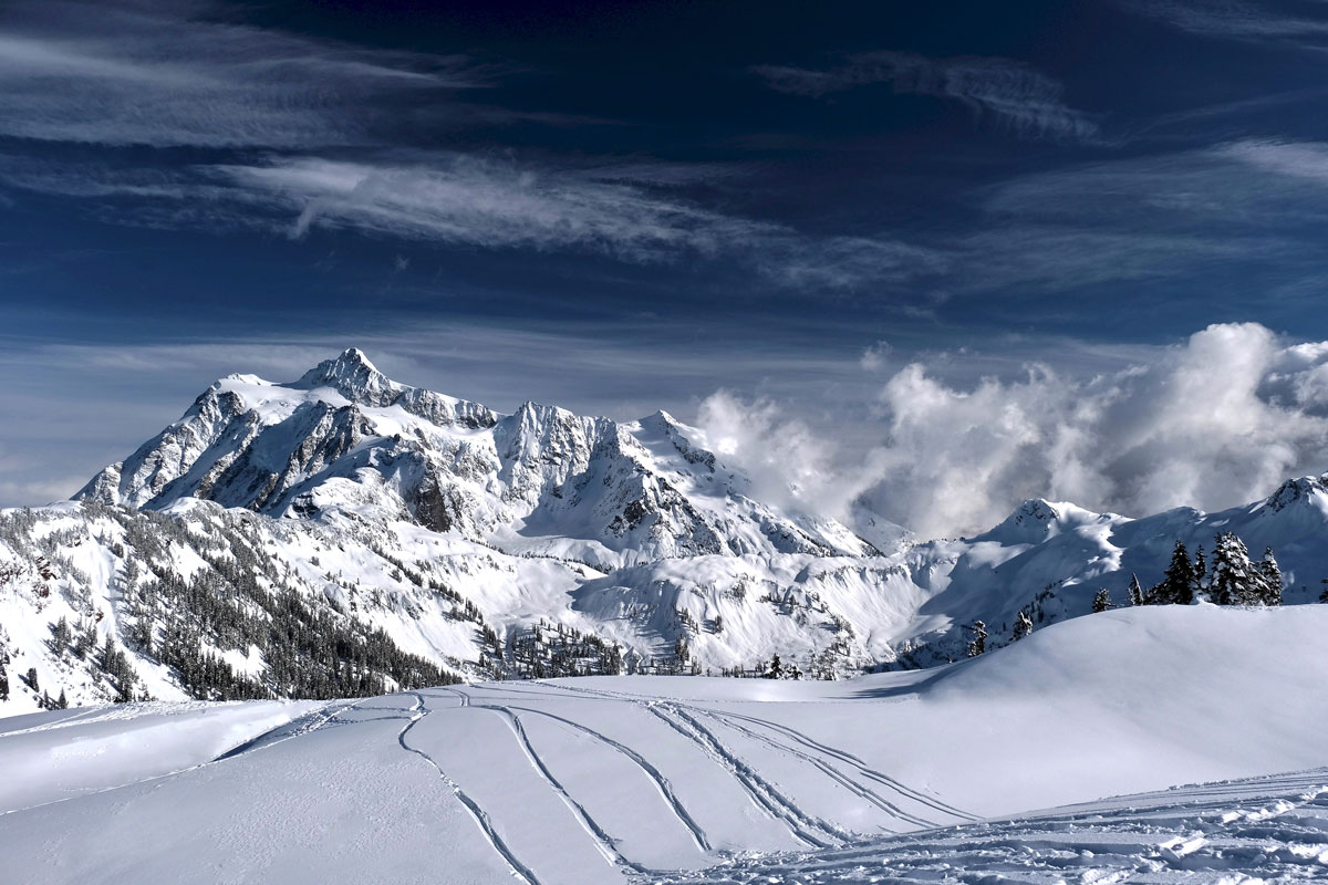 ski tracks on fresh powder snow with high mountains peaks in distance